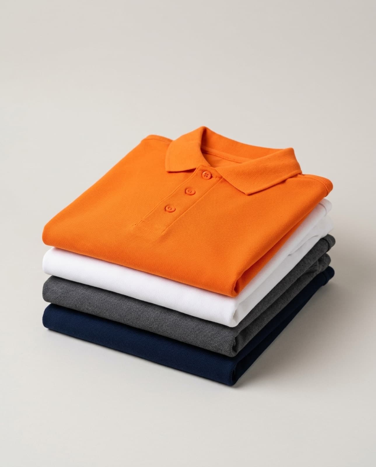 Polos piqué doblados en azul marino, gris, blanco y naranja, colores corporativos (imagen ilustrativa)